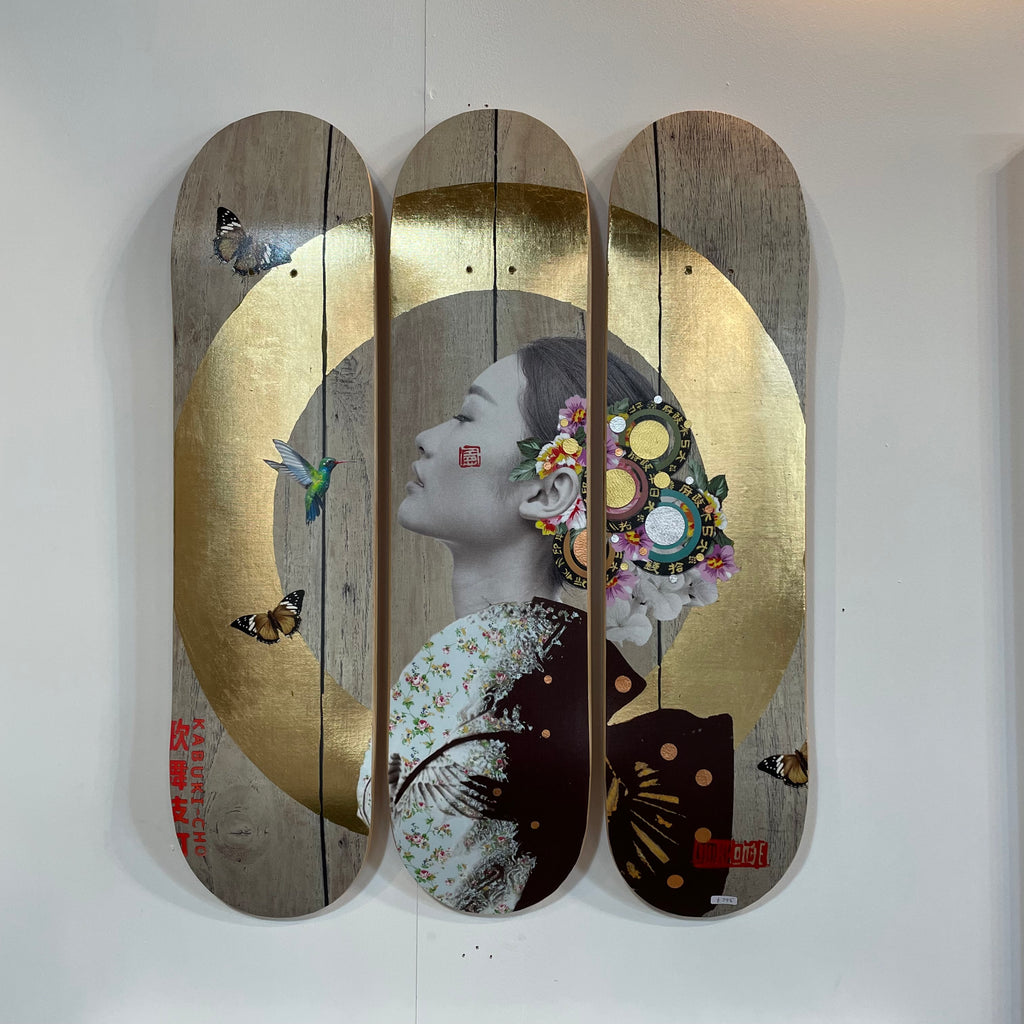 Gold leaf painting of an Asian woman with white face paint and Japanese-style logos, looking away, set against a background of used skateboards and with butterflies around her
